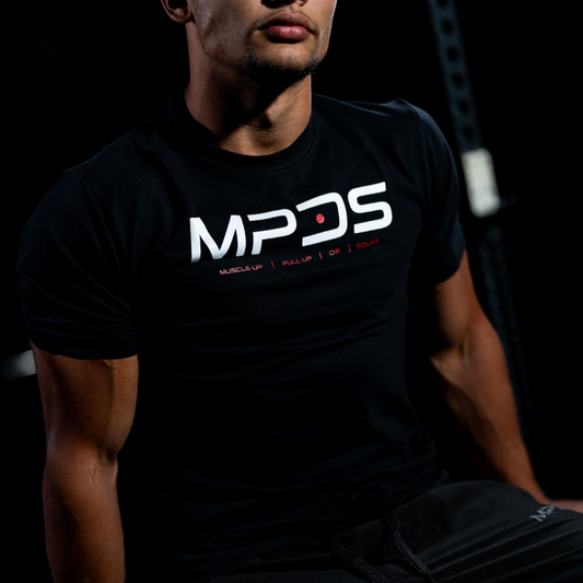 Person wearing a black t-shirt with 'MPDS' logo sitting on a wooden block against a dark background